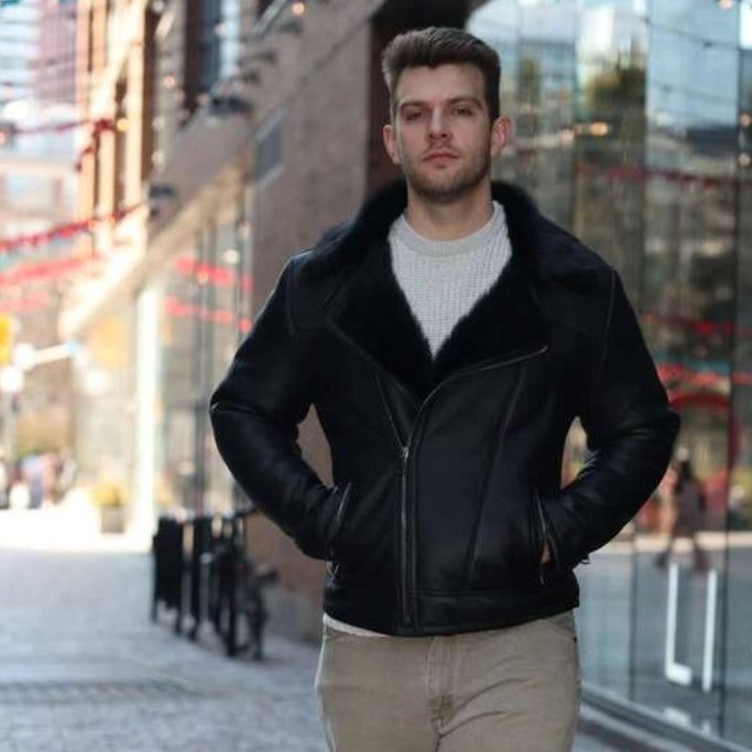 Man wearing a black leather jacket and beige pants walking on a city street.