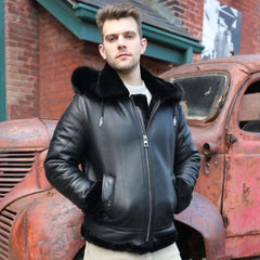 Man in a black leather jacket standing in front of an old rusted truck.