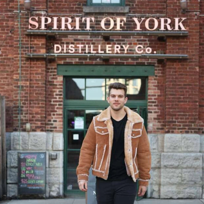 Man in a brown jacket standing in front of 'Spirit of York Distillery Co.'