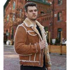 Man wearing a brown shearling jacket in an urban setting with brick buildings.