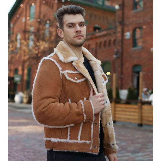 Man wearing a brown shearling jacket in an urban setting with brick buildings.