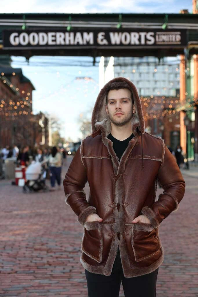 Person wearing a brown leather coat with fur trim in an urban setting with 'Gooderham & Worts Limited' sign.