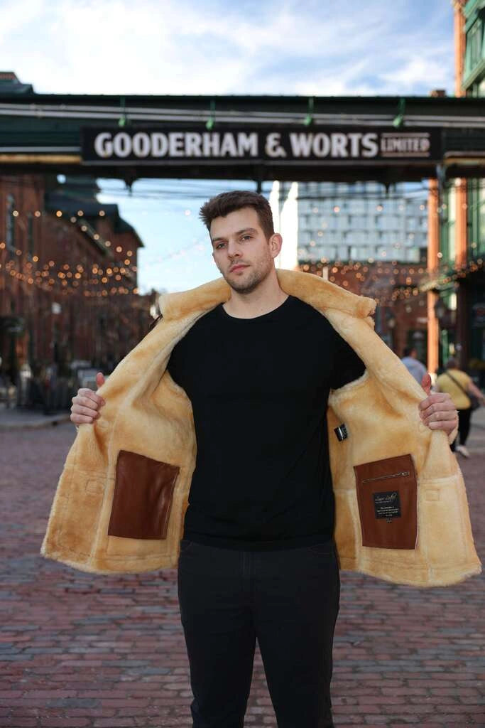 Man wearing a yellow coat with brown patches in an urban setting with 'Gooderham & Worts' sign.
