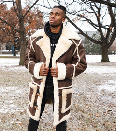 Man wearing a brown and white shearling coat in a snowy park setting