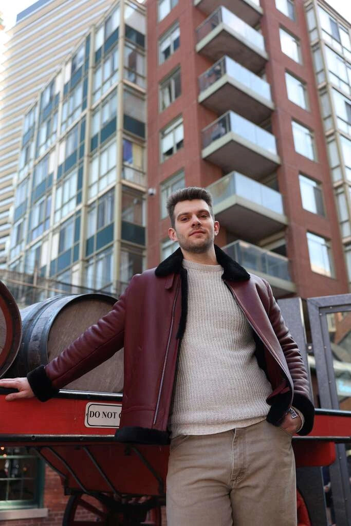 Man in Aurelius Burgundy B3 Bomber Jacket standing in front of a building with a red cart.