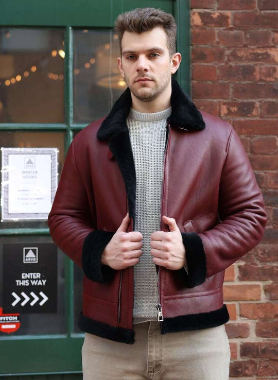 Man wearing Aurelius Burgundy B3 Bomber Jacket with black fur lining in front of a brick wall.