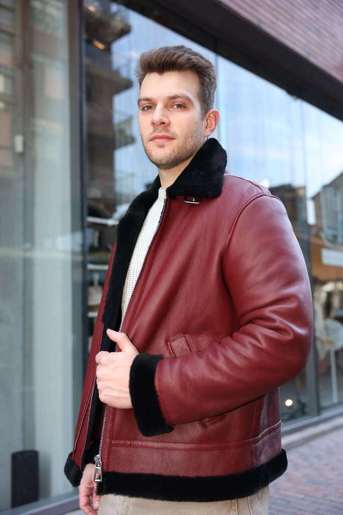 Man wearing Aurelius Burgundy B3 Bomber Jacket with black trim standing in front of a glass building.
