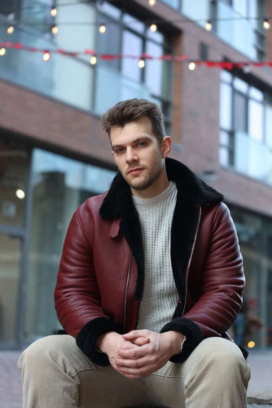 Man wearing Aurelius Burgundy B3 Bomber Jacket with fur lining sitting in an urban setting.