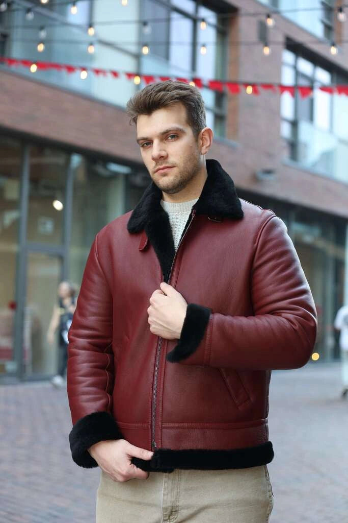 Man wearing Aurelius Burgundy B3 Bomber Jacket with black fur trim zippers closed in an urban setting.