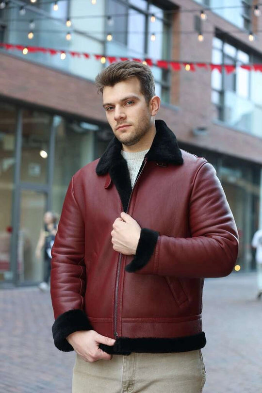 Man wearing Aurelius Burgundy B3 Bomber Jacket with black fur trim zippers closed in an urban setting.