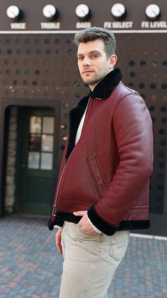 Man wearing Aurelius Burgundy B3 Bomber Jacket with black fur trim standing in front of an amplifier.