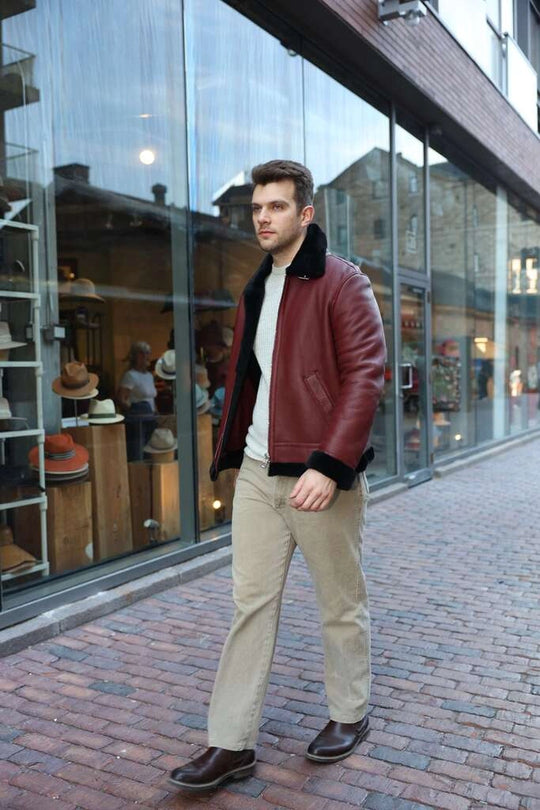 Man in Aurelius Burgundy B3 Bomber Jacket walking on a brick sidewalk with a store in the background