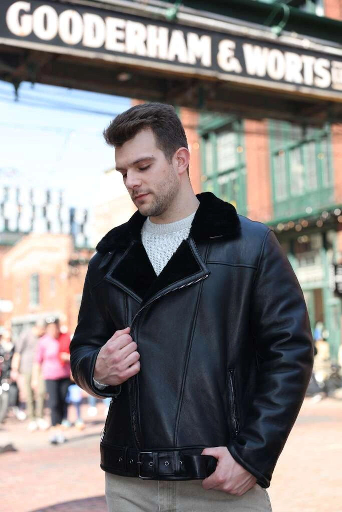 Man wearing a Black on Black Belted Shearling Leather Biker Jacket in front of a building with 'Gooderham & Worts' sign.
