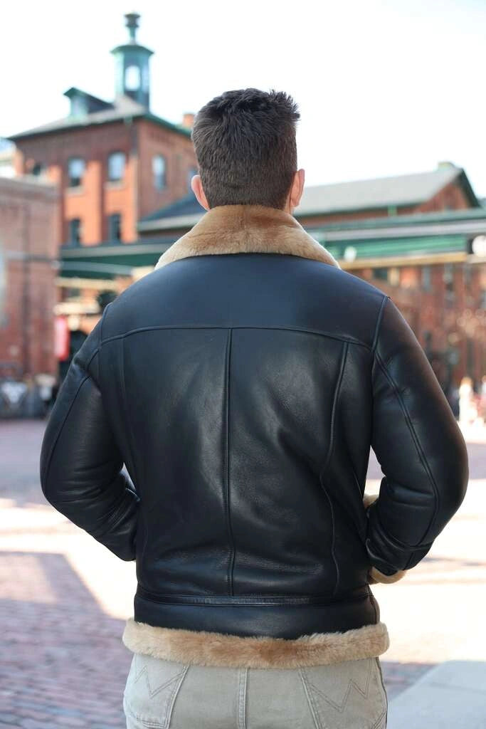 Back view of a Person wearing classic ginger brown b3 bomber shearling  black leather jacket with fur collar in an urban setting