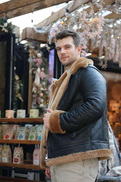 Man wearing Classic Ginger Brown B3 Bomber Aviator Shearling Jacket with brown fur trim in an indoor setting with decorative lights.