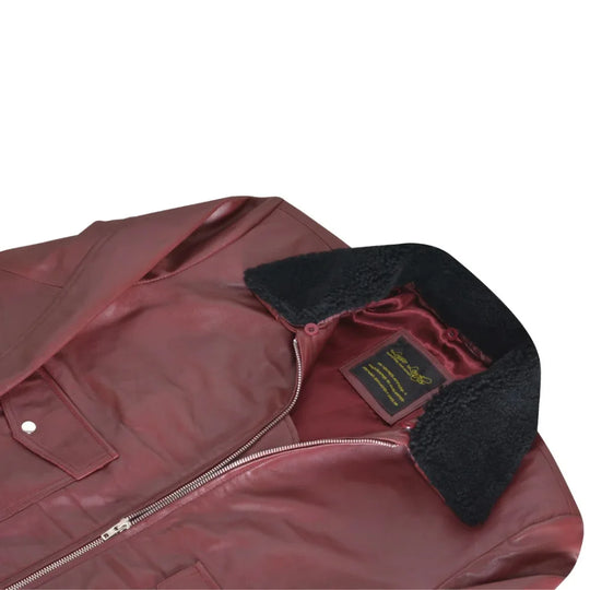 Close-up of Justin's burgundy bomber jacket laid flat, showing the black fur collar, interior brand label, and smooth satin-finish lining on white background.