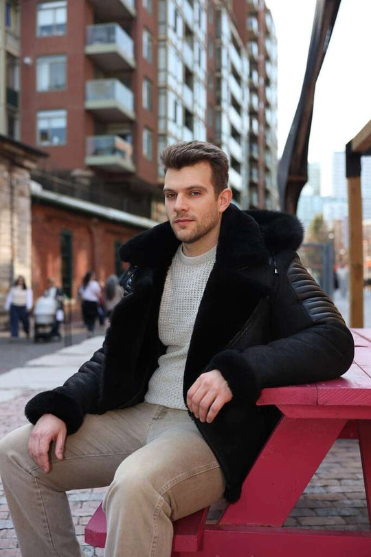 Man wearing Lucas Black Aviator Bomber Shearling Jacket with Hoodie, sitting on a red bench in an urban setting