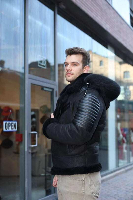 Man wearing Lucas Black Aviator Bomber Shearling Jacket with Hoodie standing in front of a glass building.