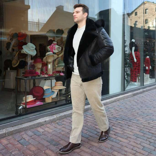 Man wearing Lucas Black Aviator Bomber Shearling Jacket with Hoodie walking on a street with a store window display in the background