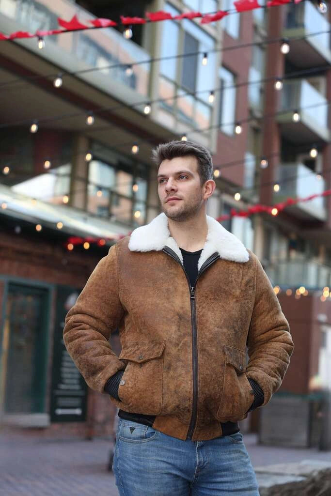 Man wearing Lucian's distressed brown A2 Bomber shearling jacket with white fur lining in an urban setting.