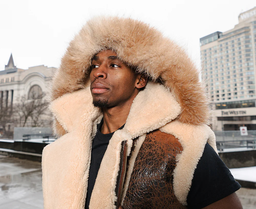 Outdoor lifestyle shot of a model wearing Ridgeway's Brown Shearling Vest, made from distressed leather with white shearling trim. The model stands in an urban outdoor setting, with the vest providing both warmth and rugged style.