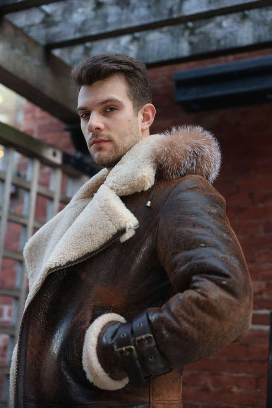 Man wearing Rocco vintage brown aviator shearling jacket with fur trim standing in front of a brick wall.